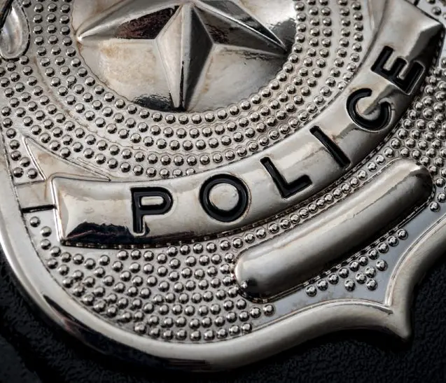 Frame 1618874302 (1) (1) Silver police badge close-up on black background.